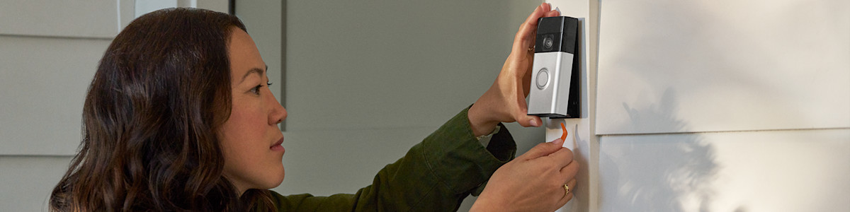 Hands installing a Ring Video Doorbell on a white wall