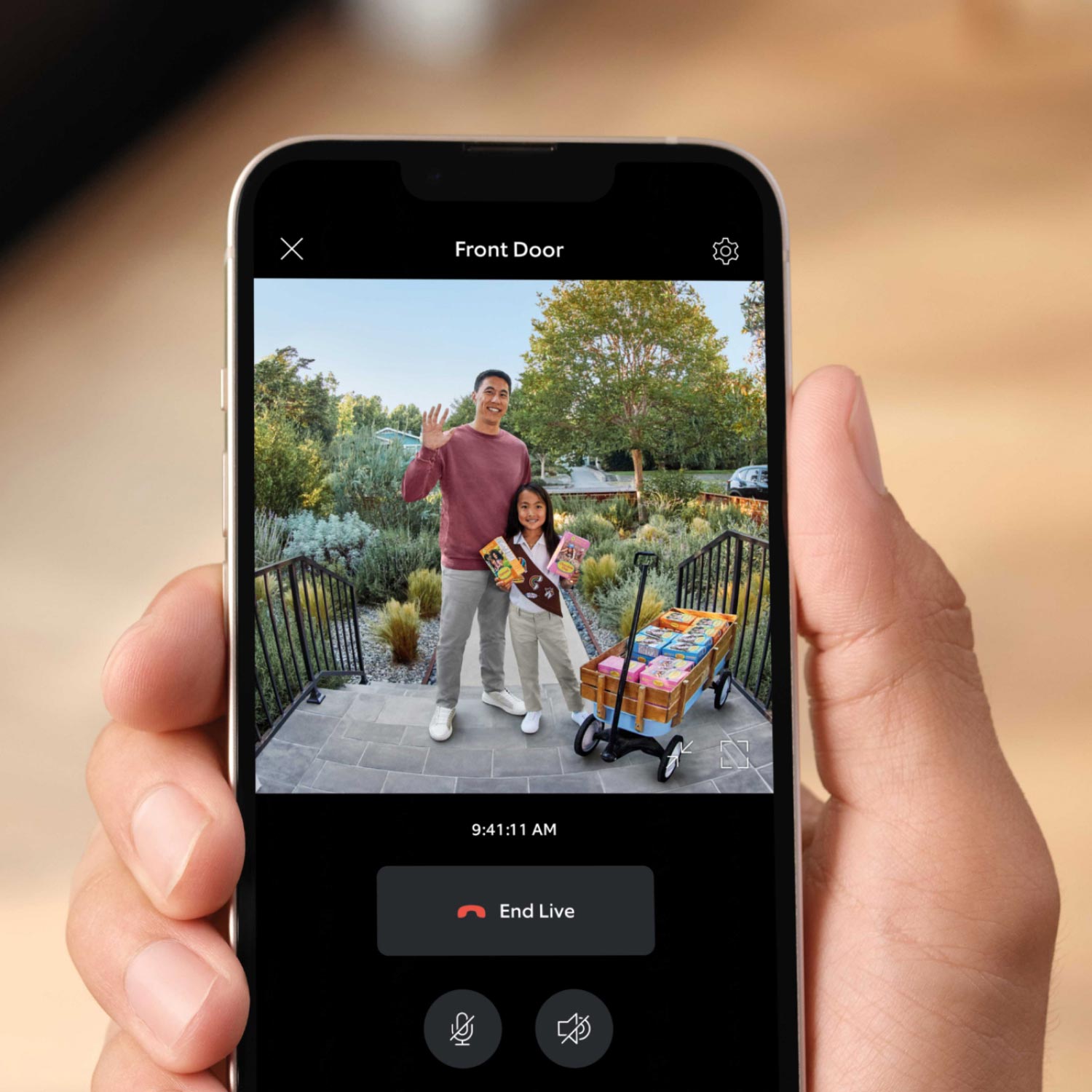 Battery Doorbell Plus (Video Doorbell) (Certified Refurbished) - Hand holding a smartphone showing a live Ring video feed of a waving man and child on a front porch selling cookies.