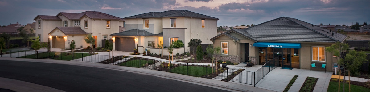 Modern suburban homes at dusk with illuminated windows and dramatic cloudy sky