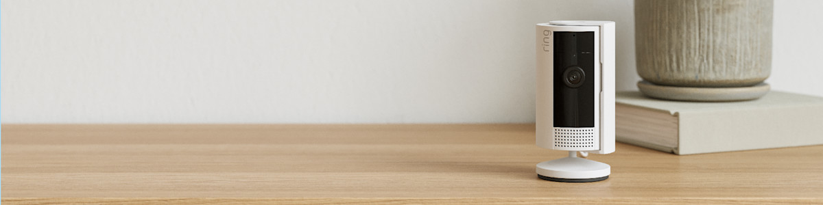Ring security camera on wooden desk with potted plant in background