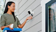 Person inserting a quick release battery into a white Ring security camera on a wall. 