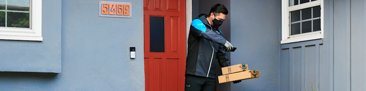 Delivery person in mask carrying Amazon parcels at red door